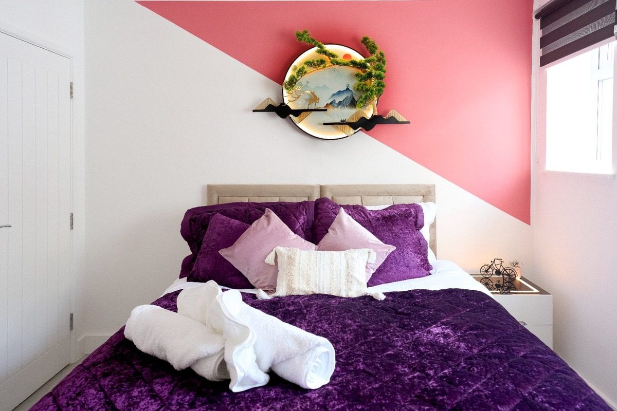 Double bed dressed in purple velvet beneath a pink feature wall